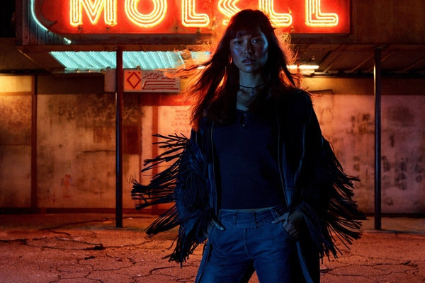 In a grainy, nocturnal frame evocative of late-70s Kodachrome film, an Indigenous woman stands firmly beneath a rattling neon motel sign whose intermittent amber glow throws jittery shadows across her angular features. Her fringed suede jacket sways slightly in a warm breeze, the delicate tassels catching glimmers of flickering light like whispered accents. The tough-yet-feminine curves of her dark denim bell bottoms contrast the coarse texture of cracked asphalt and peeling paint behind her, grounding her stance in a roadside Americana tableau.

Her face emerges partially cloaked in shadow, the chiaroscuro contouring her high cheekbones with soft, muted dusk hues and elusive cigarette-smoke blue tints. Her gaze is steady, infused with a wistful edge — an interplay of resilience and vulnerability that captures a whispered story beneath the urban solitude. Hair softly tousled and natural, it catches stray neon strands with a subtle sheen, textured by the analog grain that imbues the entire image with tactile authenticity.

The low-angle 28mm lens skews perspective just slightly, emphasizing her quiet strength and tethering the frame between intimate portraiture and environmental storytelling. The flickering light sculpts the motel’s weathered wooden facade and rusty metal fixtures behind her, amplifying an atmosphere charged with late-night anticipation and vintage nostalgia.

Every element, from flickering sodium-vapour illumination to mottled skin pores and the jangling sway of fringe, pulses with textured realism. The color palette carries warm amber highlights, cool blues of shadow, and earthen tones that evoke dusty roadside dreams. This precise cinematic tableau spaces emotion and time, balanced with thoughtful composition and authentic 35mm film grain.

—late-70s / early-80s cinematic photograph, authentic film grain.