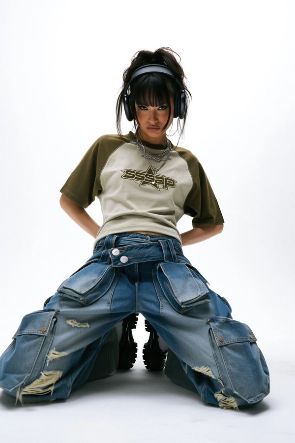 She’s kneeling in a minimalist white studio backdrop, the shot framed from a low mid-angle that tilts slightly upward amplifying her commanding stance. She sports a raglan tee in earthy brown and olive green with a retro star logo stamped “sssap” across the chest as a perfect Y2K throwback. Her oversized, wide-leg denim cargos show heavy distressing and large pockets that hang loosely, paired with chunky black streetwear shoes grounding the look. Her messy ponytail pulls back loose strands that soften her rebellious, piercing glare. Large black wired headphones rest heavily atop her head, injecting a sharp cyber edge. The soft, even studio light crisply reveals fabric textures and creases, while subtle shadows add depth to the pristine white backdrop. The expression is provocative yet controlled, channeling indie sleaze mixed with Harajuku editorial attitude in a deliberate, off-kilter pose.
—casual candid early-2000s Y2K snapshot, grainy softness