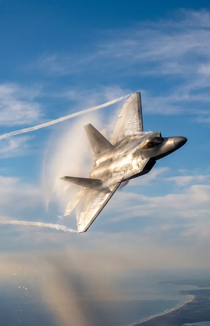 Futuristic fighter jet performing a high-speed maneuver above the coastline, vapor cones forming around the wings