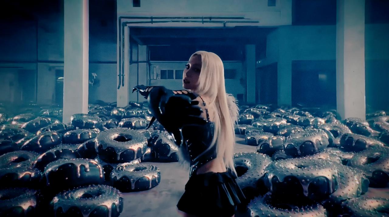 Ivy stands inside a warehouse filled with metallic forms as a glove moves through the scene. The studio explored several image and video directions on Higgsfield before selecting the shots used in the final edit.